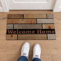 Zerbino Essential con decoro a riquadri effetto legno nei toni marrone, beige e grigio e scritta Welcome Home su fascia nera