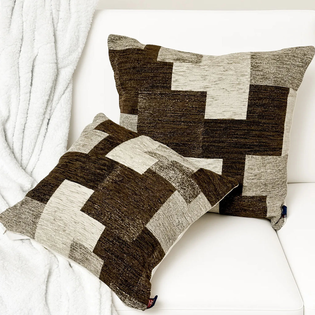 Coppia di cuscini in velluto e ciniglia con motivo patchwork geometrico marrone mélange e beige su divano bianco