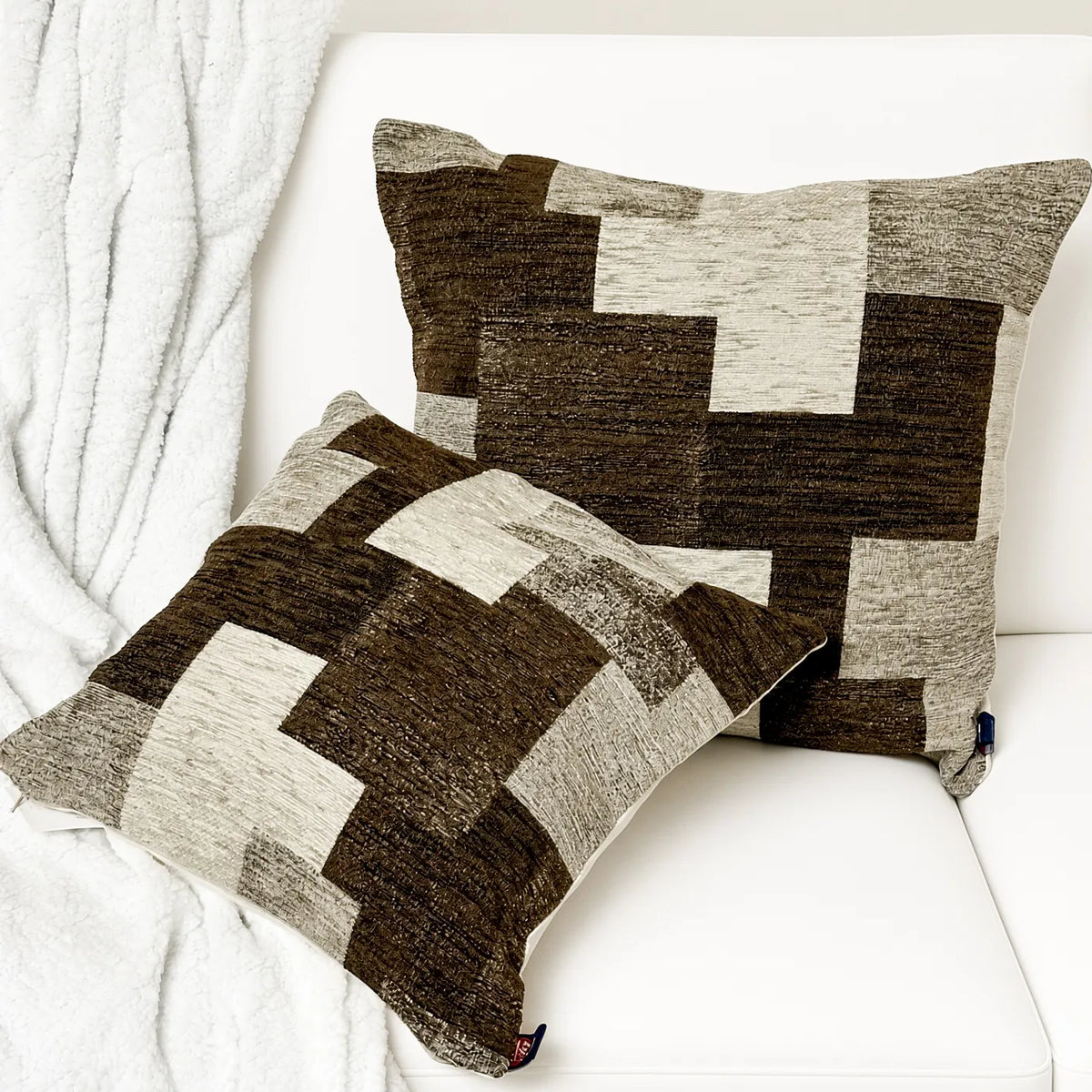 Coppia di cuscini in velluto e ciniglia con motivo patchwork geometrico marrone mélange e beige su divano bianco