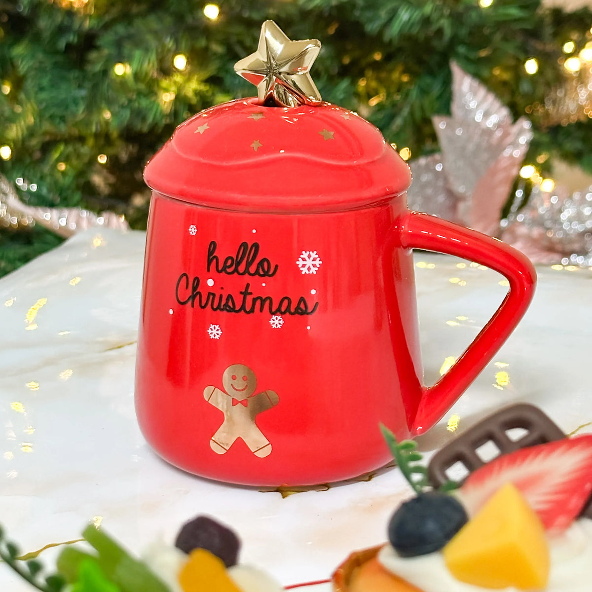 Tazza natalizia rossa con omino pan di zenzero, scritta hello Christmas e coperchio coordinato, davanti all’albero di Natale