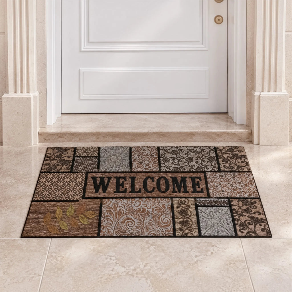 Zerbino Essential con motivi patchwork marroni, beige e grigi e scritta WELCOME davanti a una porta bianca