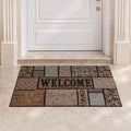 Zerbino Essential con motivi patchwork marroni, beige e grigi e scritta WELCOME davanti a una porta bianca